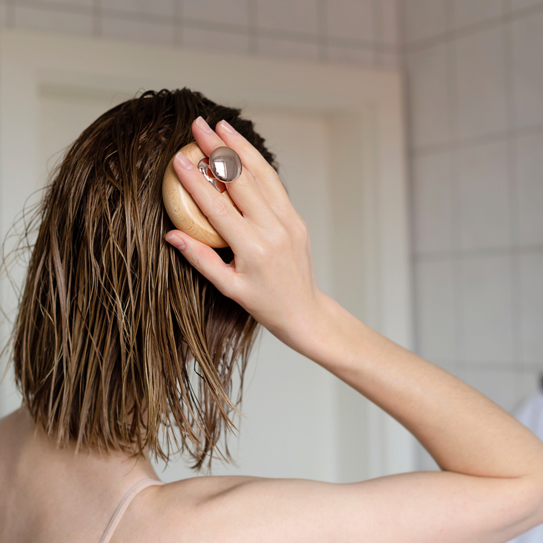 A person is captured from behind running their fingers through wet hair, a scene often associated with hair care routines and the intimate moments of self-care and reflection.