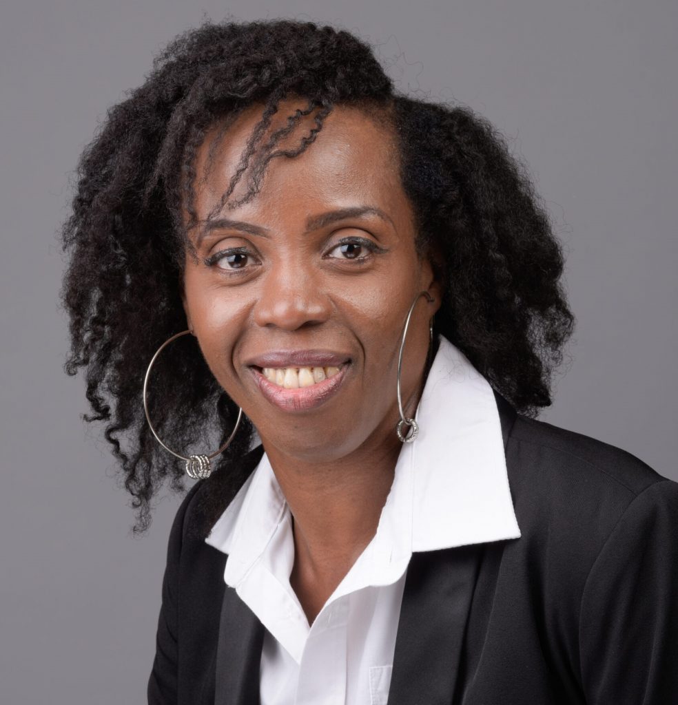 Portrait of Sophia A Marshall, the founder of Alopecia & Beyond Hair Clinic & Wellness Spa, showcasing a warm, confident smile. She is styled in professional attire with a black blazer and white shirt, accessorized with large hoop earrings, embodying her role as an experienced and certified trichologist and holistic wellness advocate.